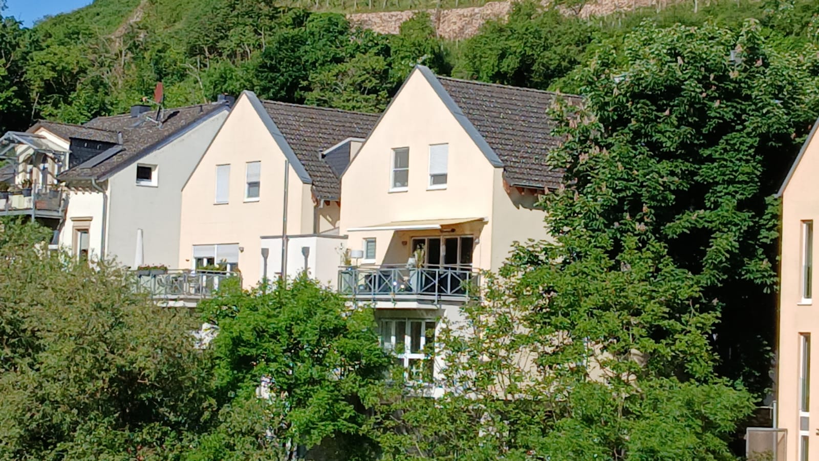 Blick auf die Maisonette-Wohnung mit Balkonen und grüner Hanglage am Wasser